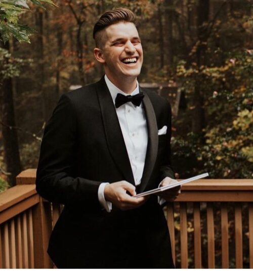 A young man laughing who is wearing a custom made black tuxedo, white shirt and black bow tie from HKT Clothiers.